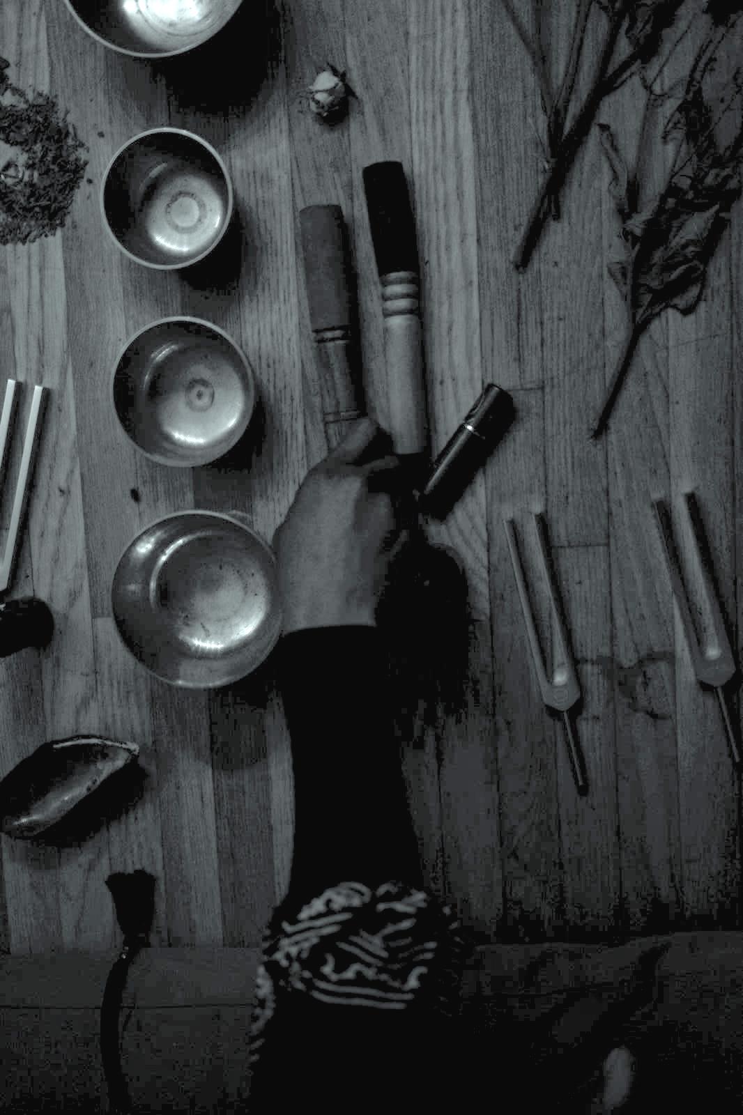 A hand reaching over a table filled with sound bowls, tuning forks, and sound healing tools